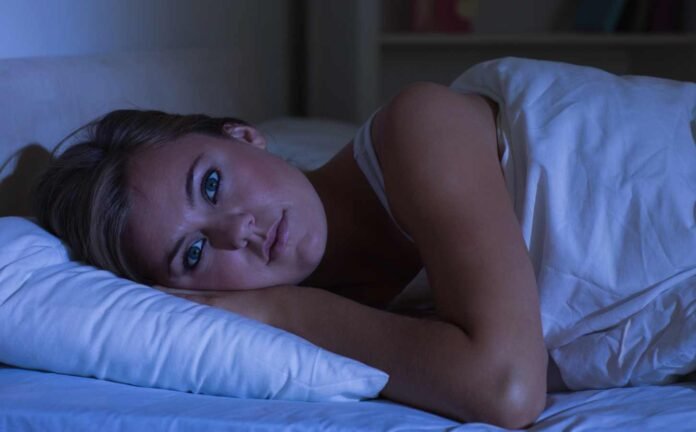 A woman in a white night dress lying awake with Insomnia.