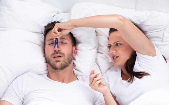 Frustrated woman trying to stop a man snoring by putting a clothes peg on his nose.